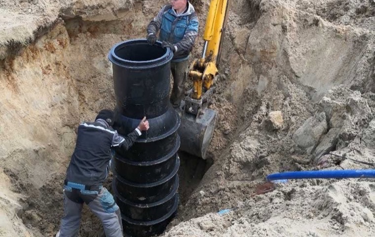 Montaż studni kanalizacyjnej w wykopie przy użyciu koparki