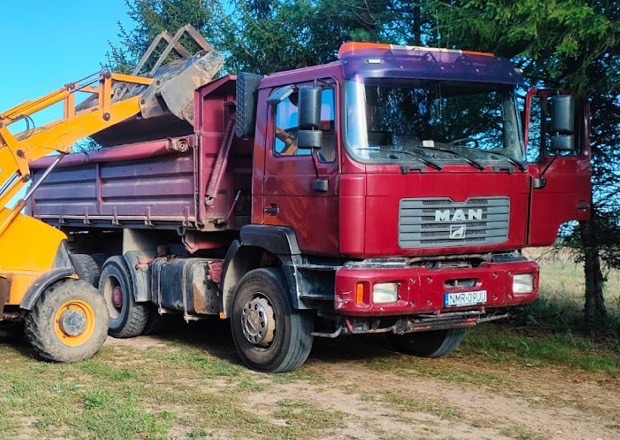 Wywrotka MAN F2000 6x4 z kabiną i skrzynią wywrotki, obok łyżka koparko-ładowarki